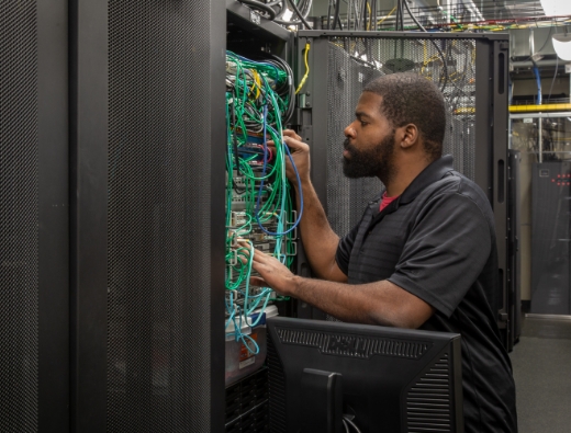 man kneels down and performs maintenance on server rack